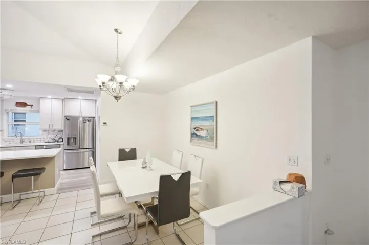 Tiled dining space featuring an inviting chandelier, lofted ceiling, and sink
