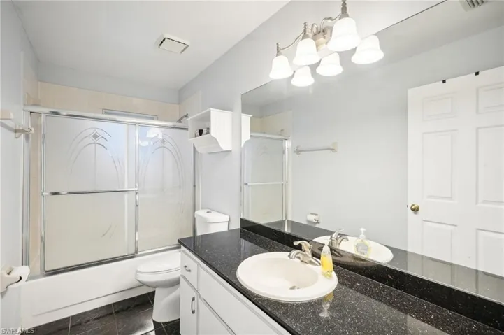 Full bathroom with shower / bath combination with glass door, an inviting chandelier, tile patterned floors, vanity, and toilet