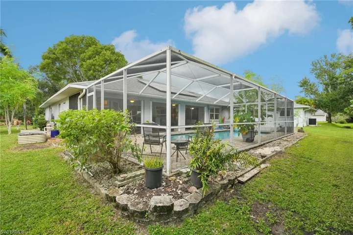 Back of house featuring glass enclosure, a patio, and a lawn