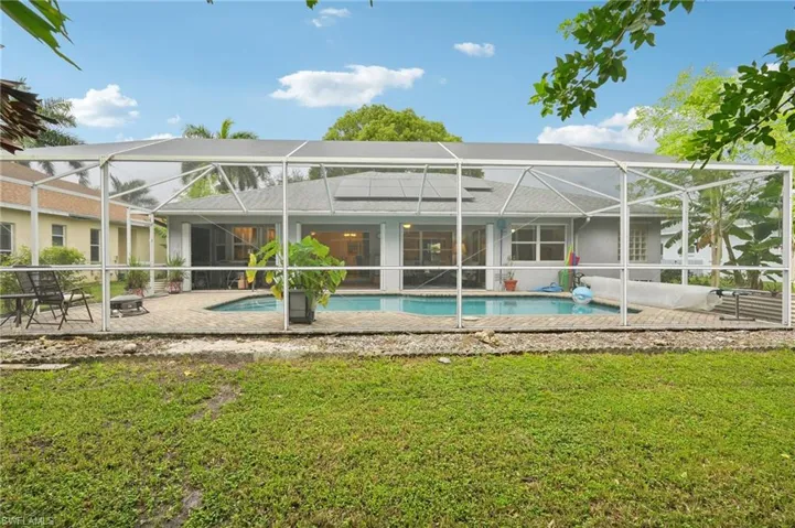 Back of house with a yard, glass enclosure, and a patio