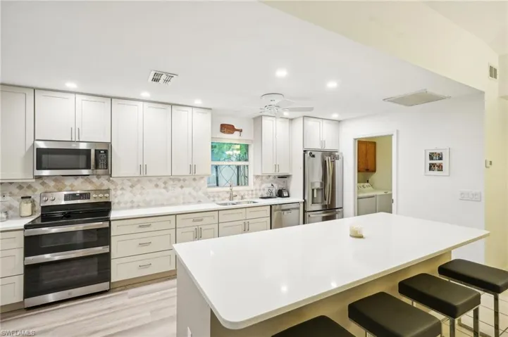 Kitchen with ceiling fan, sink, appliances with stainless steel finishes, washing machine and dryer, and a breakfast bar area