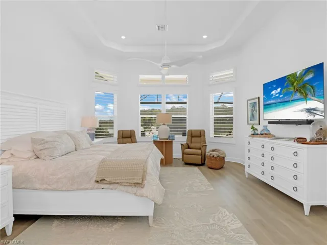 Bedroom with light wood-style flooring, a high ceiling, a raised ceiling, a ceiling fan, and recessed lighting