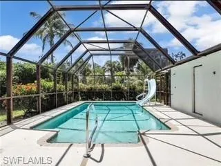 Outdoor pool featuring a water slide, a sunroom, a patio, and glass enclosure