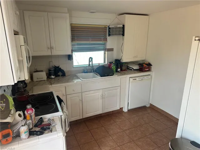Kitchen with white appliances, sink, backsplash, tile countertops, and white cabinetry