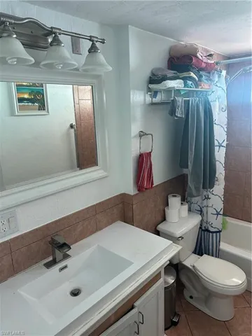 Full bathroom with vanity, tile patterned floors, shower / bathtub combination with curtain, tile walls, and toilet