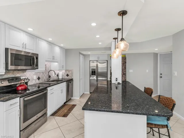Kitchen featuring white cabinetry, sink, hanging light fixtures, stainless steel appliances, and a breakfast bar area