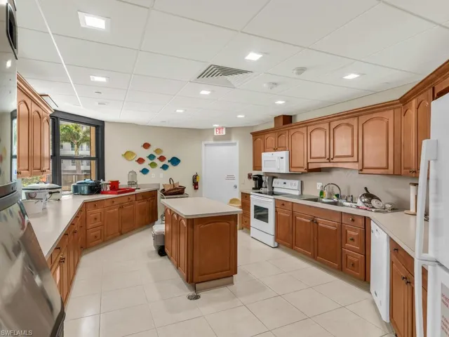 Kitchen featuring white appliances, a kitchen island, a drop ceiling, and light tile patterned flooring