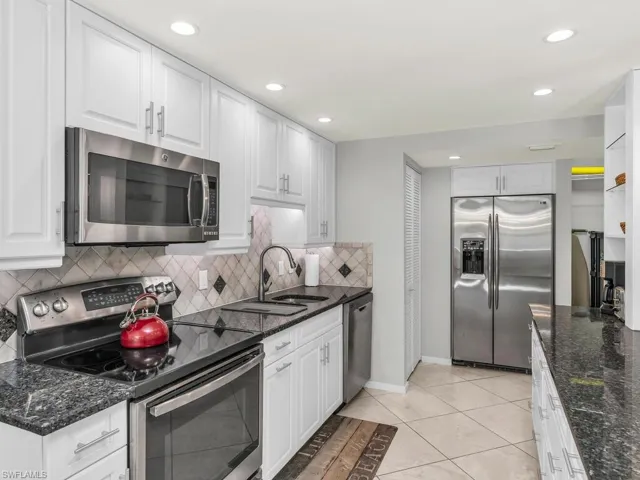 Kitchen featuring white cabinetry, sink, dark stone counters, light tile patterned floors, and appliances with stainless steel finishes