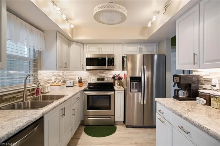 Kitchen with stainless steel appliances, rail lighting, backsplash, and white cabinetry