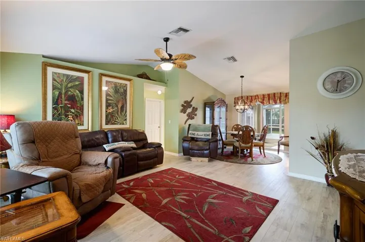 Living room with lofted ceiling, ceiling fan, wood finished floors, and a chandelier