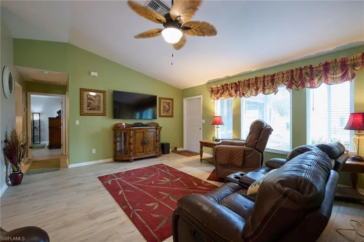 Living room featuring ceiling fan, lofted ceiling, and light wood-style floors