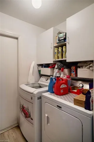 Laundry room with independent washer and dryer, light wood-type flooring, and cabinet space