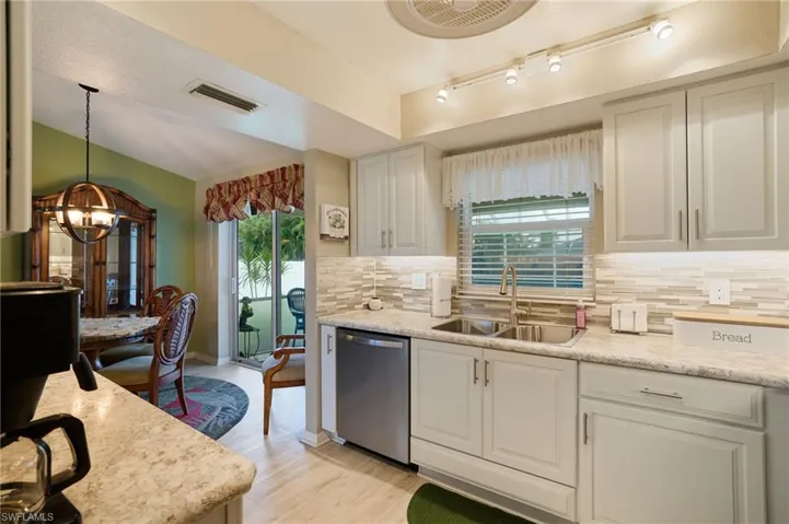 Kitchen featuring stainless steel dishwasher, a chandelier, light wood-style flooring, backsplash, and white cabinetry