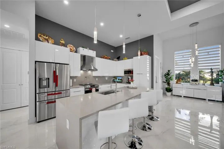 Kitchen with appliances with stainless steel finishes, tasteful backsplash, light marble finish floors, white cabinets, and decorative light fixtures