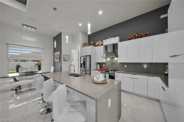 Kitchen with a kitchen breakfast bar, modern cabinets, wall chimney range hood, white cabinets, and a center island with sink