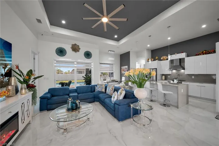 Living area with a glass covered fireplace, light marble finish flooring, a towering ceiling, a raised ceiling, and recessed lighting