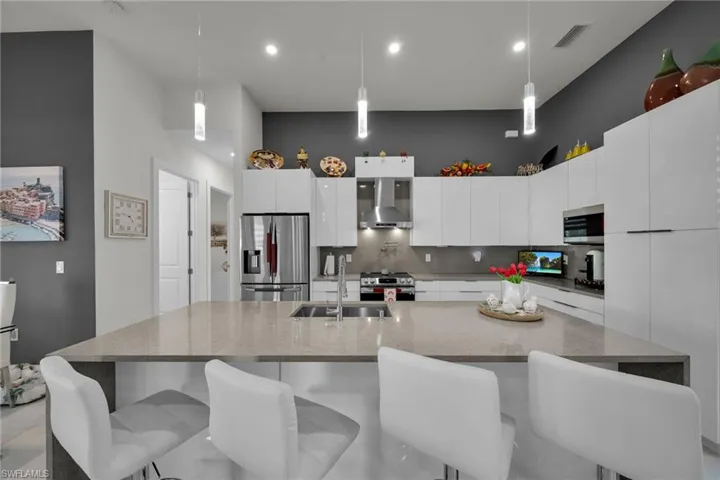 Kitchen featuring modern cabinets, tasteful backsplash, light stone countertops, decorative light fixtures, and a towering ceiling