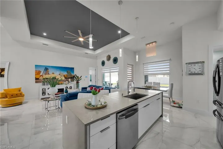 Kitchen with modern cabinets, a raised ceiling, ceiling fan, light marble finish flooring, and white cabinets