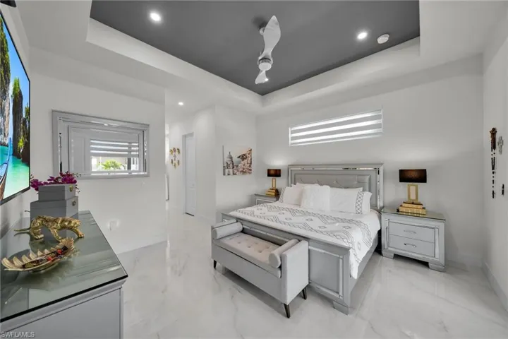Bedroom featuring a raised ceiling, light marble finish flooring, recessed lighting, and a ceiling fan