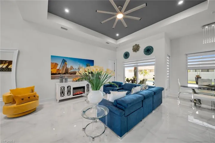 Living room with a raised ceiling, marble tiled flooring, a glass covered fireplace, a towering ceiling, and ceiling fan