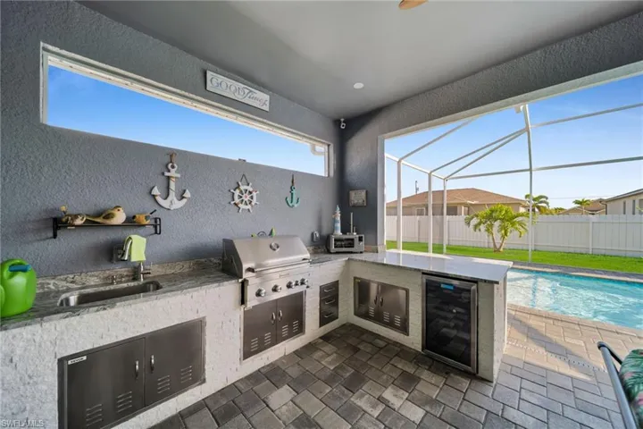 View of patio featuring a sunroom, beverage cooler, glass enclosure, and an outdoor kitchen