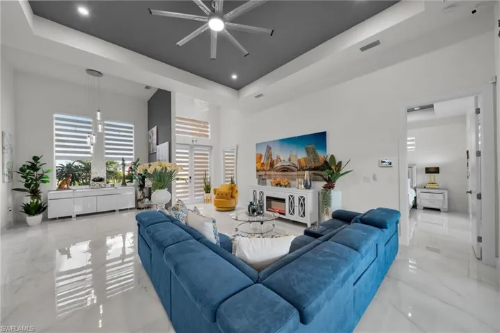 Living area featuring a raised ceiling, light marble finish flooring, ceiling fan, a high ceiling, and recessed lighting