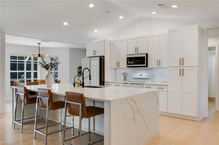 Kitchen with a center island with sink, a breakfast bar, light wood-style flooring, white cabinetry, and white electric range