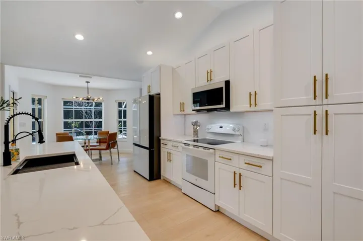 Kitchen with white range with electric stovetop, white cabinets, stainless steel microwave, freestanding refrigerator, and light stone countertops