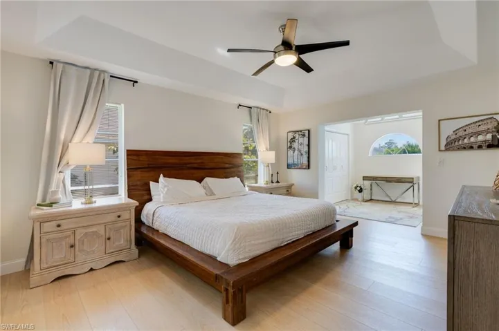 Bedroom featuring a tray ceiling, light wood finished floors, multiple windows, and ceiling fan