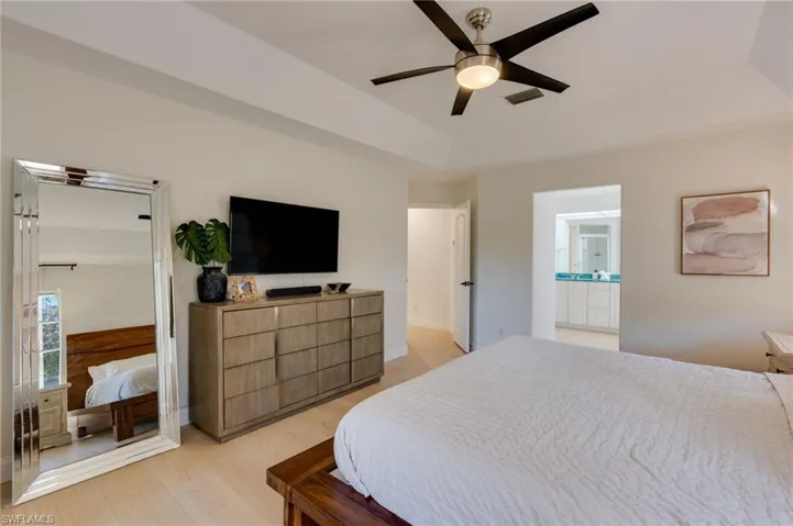 Bedroom with a raised ceiling, light wood-style floors, and a ceiling fan