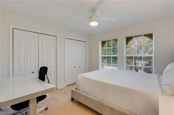 Bedroom with multiple closets, light wood finished floors, ceiling fan, and a desk