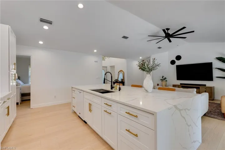 Kitchen with white cabinetry, a spacious island, light stone countertops, open floor plan, and light wood-type flooring