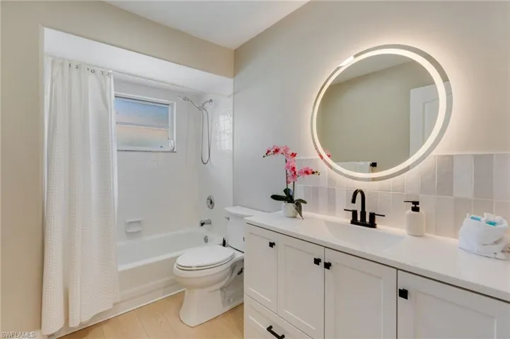 Bathroom with vanity, shower / bathtub combination with curtain, light wood finished floors, and decorative backsplash