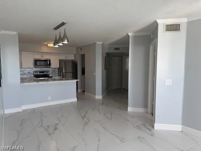 Kitchen featuring ornamental molding, light countertops, stainless steel appliances, white cabinetry, and open floor plan