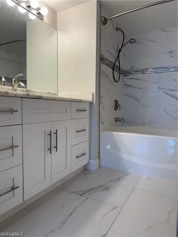 Primary Bathroom with shower / bath combination, vanity, and light marble finish flooring