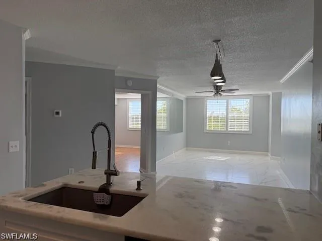Kitchen with ornamental molding, light marble finish floors, light stone countertops, a textured ceiling, and ceiling fan