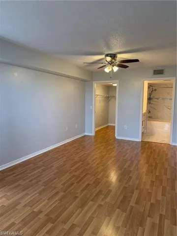 Primary bedroom featuring a textured ceiling, a spacious closet, wood finished floors, a ceiling fan, and ensuite bathroom