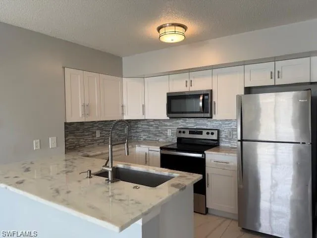 Kitchen featuring stainless steel appliances, white cabinetry, light stone counters, tasteful backsplash, and a textured ceiling