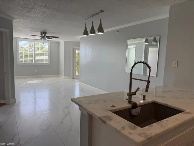 Kitchen featuring light marble finish flooring, a textured ceiling, ornamental molding, light stone countertops, and a ceiling fan