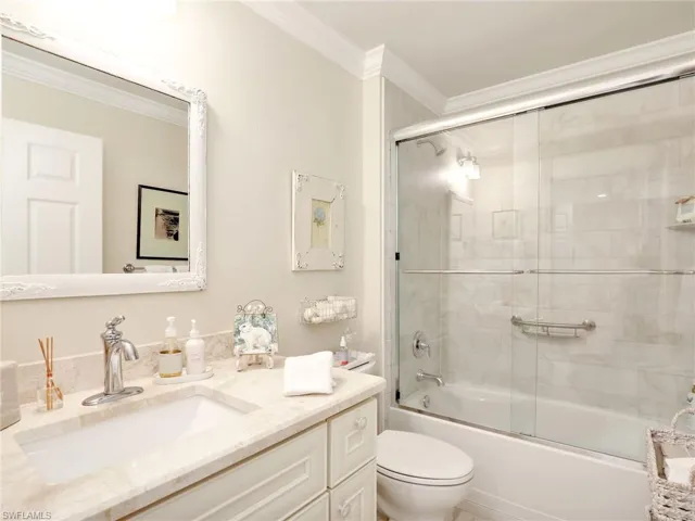 Full bathroom featuring combined bath / shower with glass door, vanity, toilet, and crown molding