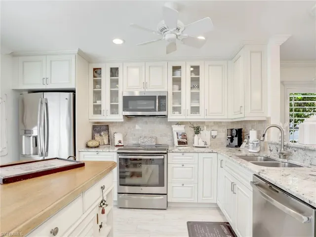 Kitchen featuring appliances with stainless steel finishes, white cabinets, backsplash, sink, and ceiling fan