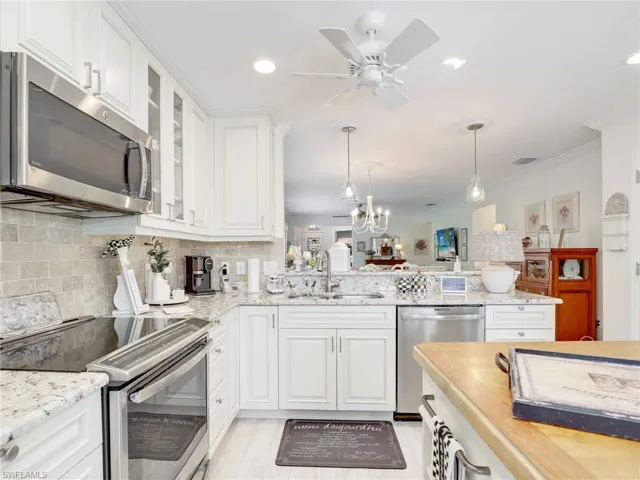 Kitchen featuring appliances with stainless steel finishes, white cabinets, kitchen peninsula, sink, and tasteful backsplash
