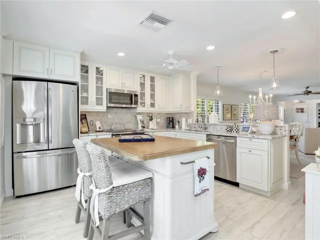 Kitchen with stainless steel appliances, ceiling fan with notable chandelier, backsplash, hanging light fixtures, and a center island
