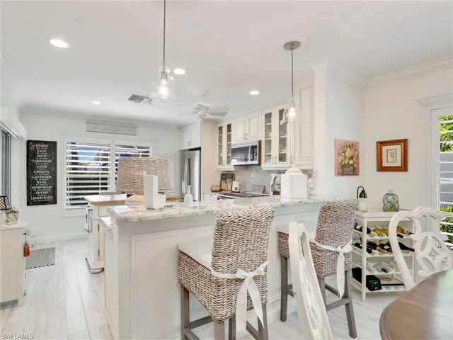 Kitchen featuring hanging light fixtures, light stone counters, white cabinets, and appliances with stainless steel finishes