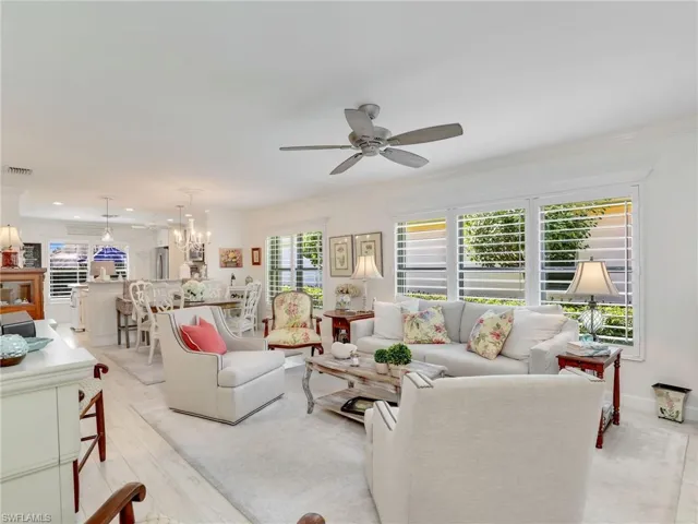 Living room with light hardwood / wood-style floors, a wealth of natural light, ornamental molding, and ceiling fan with notable chandelier