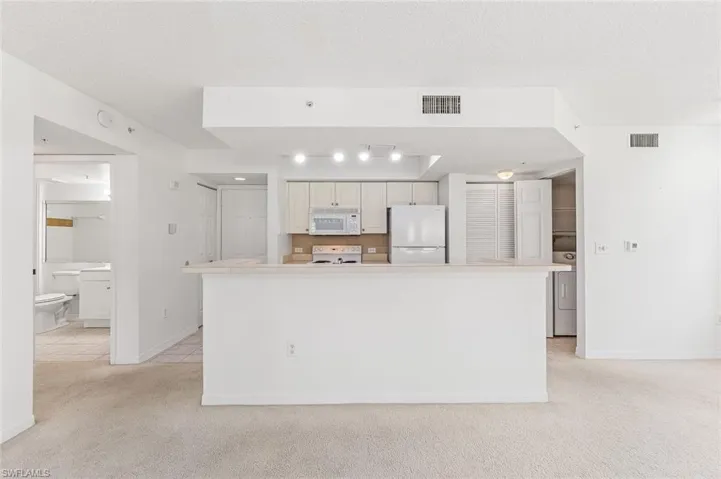 Kitchen with an eat-at counter, light cabinetry, white appliances, and a tiled backsplash, and tile floors in the kitchen and carpet in the living areas.