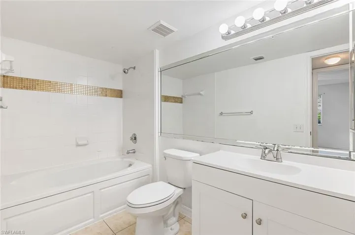 Bathroom featuring a white vanity with integrated sink, chrome faucet, and a full-width mirror, tub/shower combo, and tile flooring.