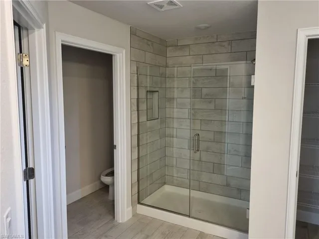 Bathroom with toilet, an enclosed shower, and hardwood / wood-style floors