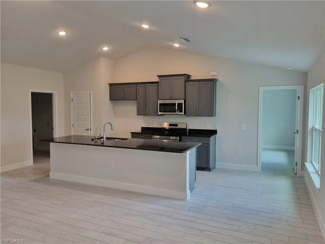 Kitchen featuring light hardwood / wood-style flooring, an island with sink, stainless steel appliances, sink, and high vaulted ceiling