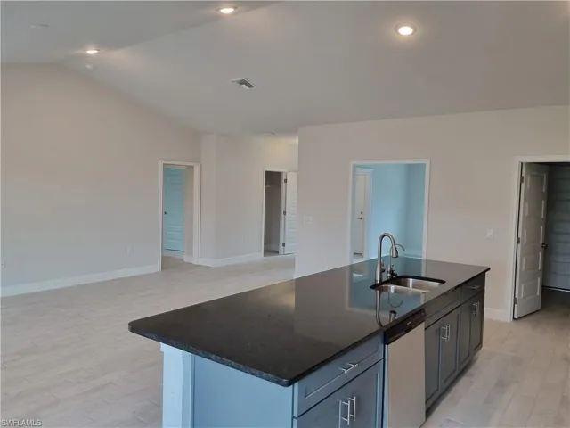 Kitchen featuring lofted ceiling, light wood-type flooring, dishwasher, sink, and a center island with sink